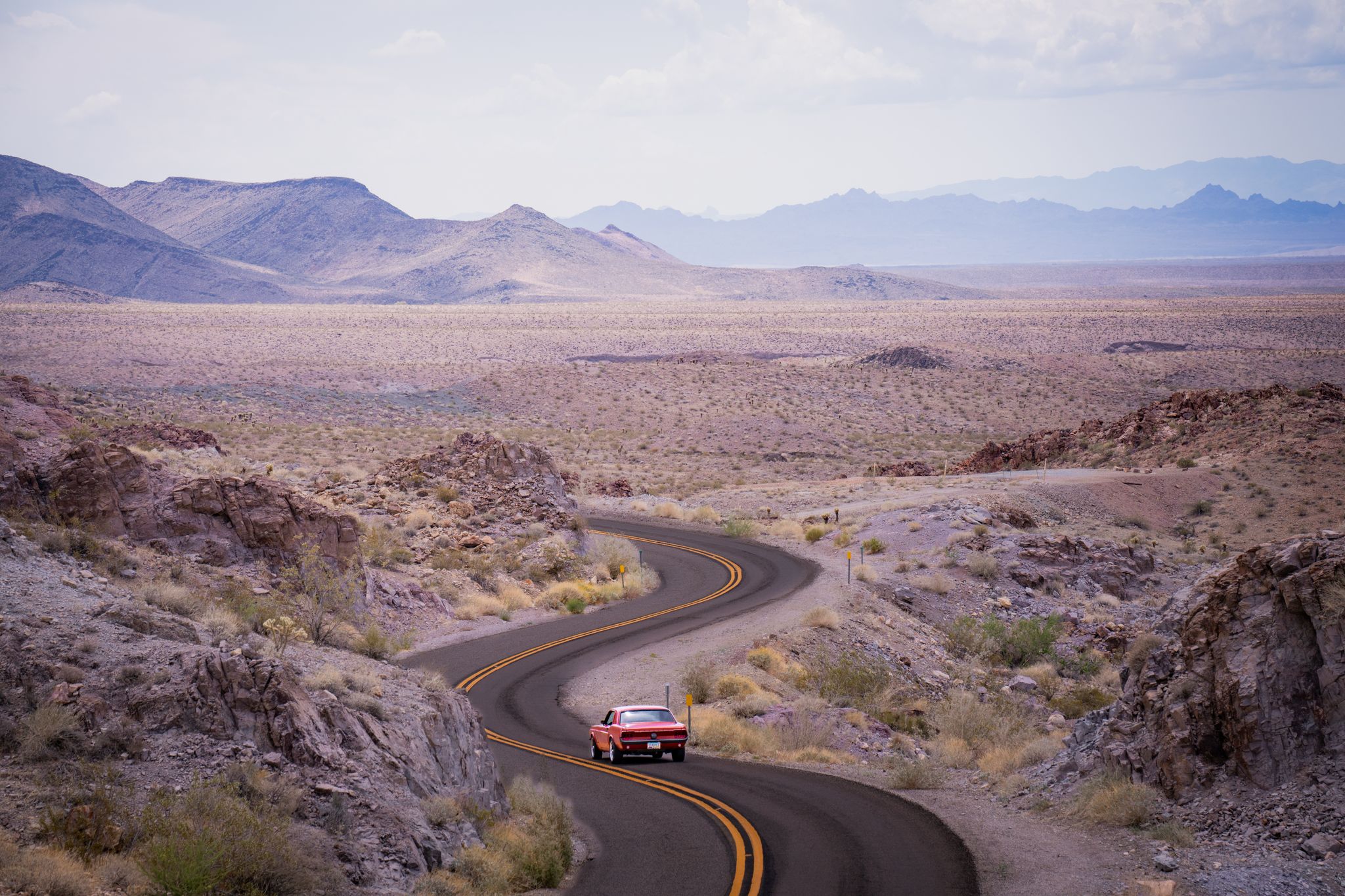 A red Mustang following a winding road through the desert