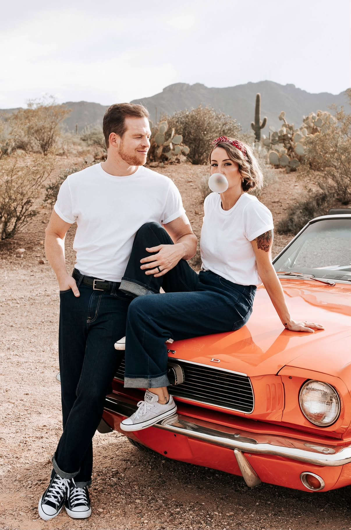 Couple posing beside the red Mustang as the woman blows bubblegum