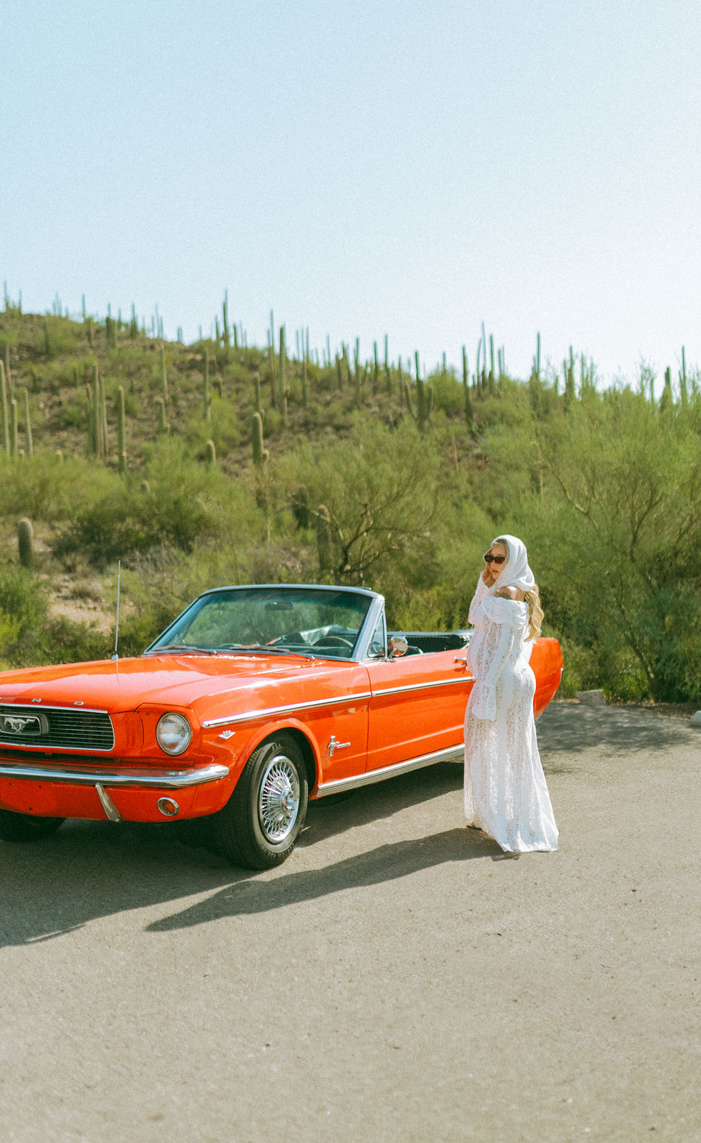 Woman in white posing beside the red Mustang Convertible in the Tucson desert