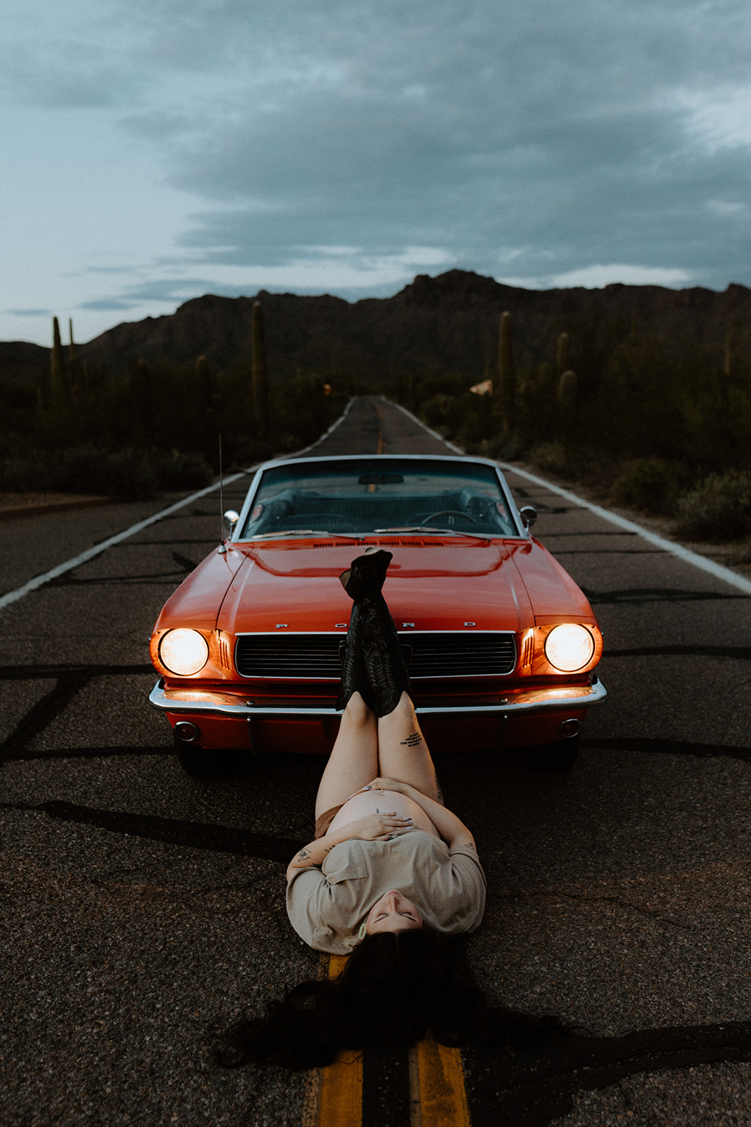 Creative maternity portrait with the red Mustang on a desert road