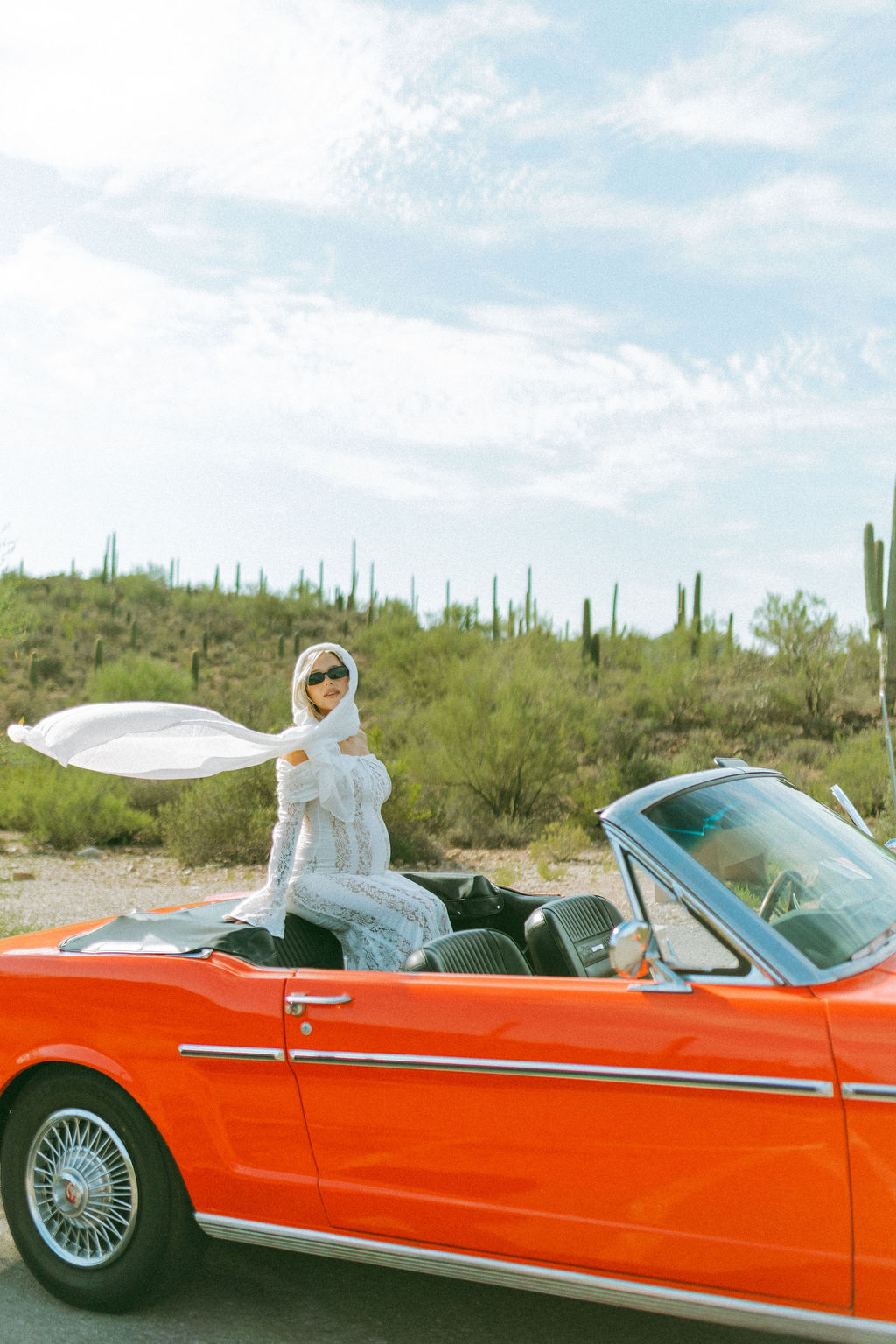 Expectant mother in white seated in the red Mustang Convertible in the Tucson desert