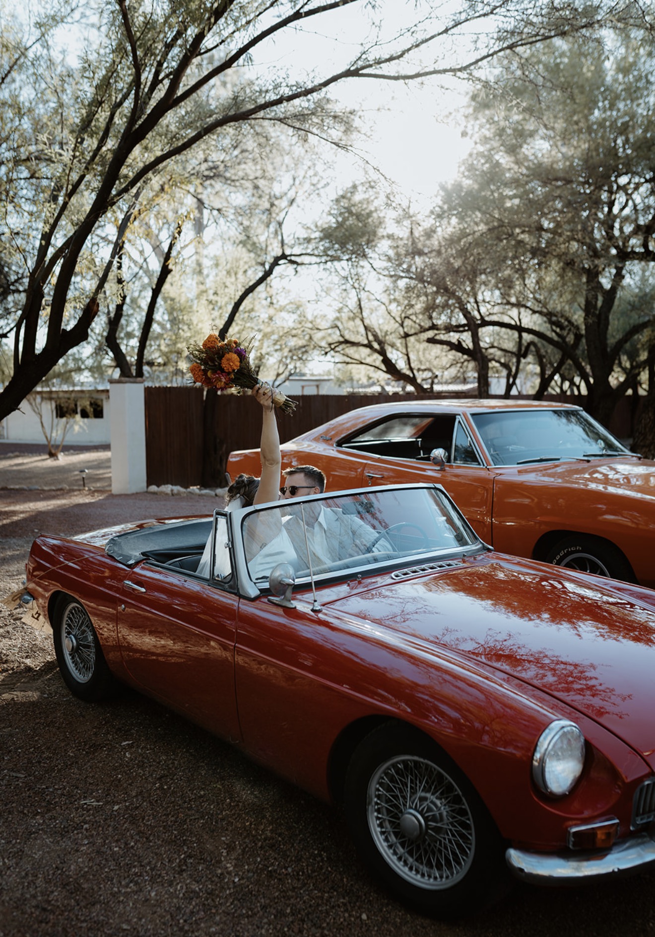 Wedding couple in a maroon MG with the orange Charger behind them